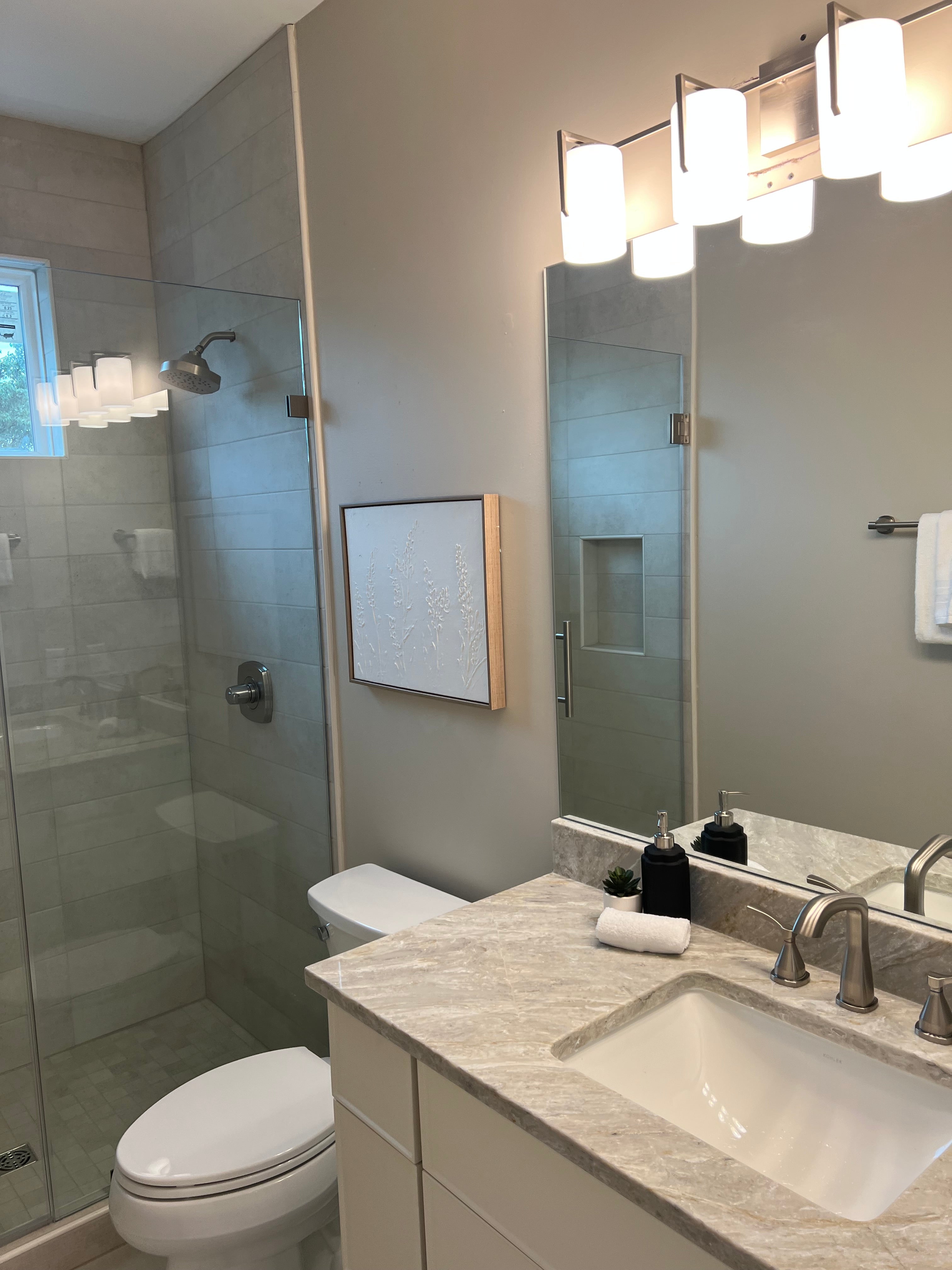 Bathroom interior with vanity, mirror, toilet, porcelain tile, and brushed nickel faucet.