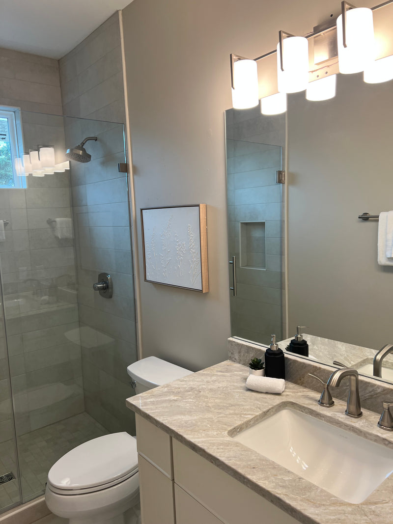 Bathroom interior with vanity, mirror, toilet, porcelain tile, and brushed nickel faucet.