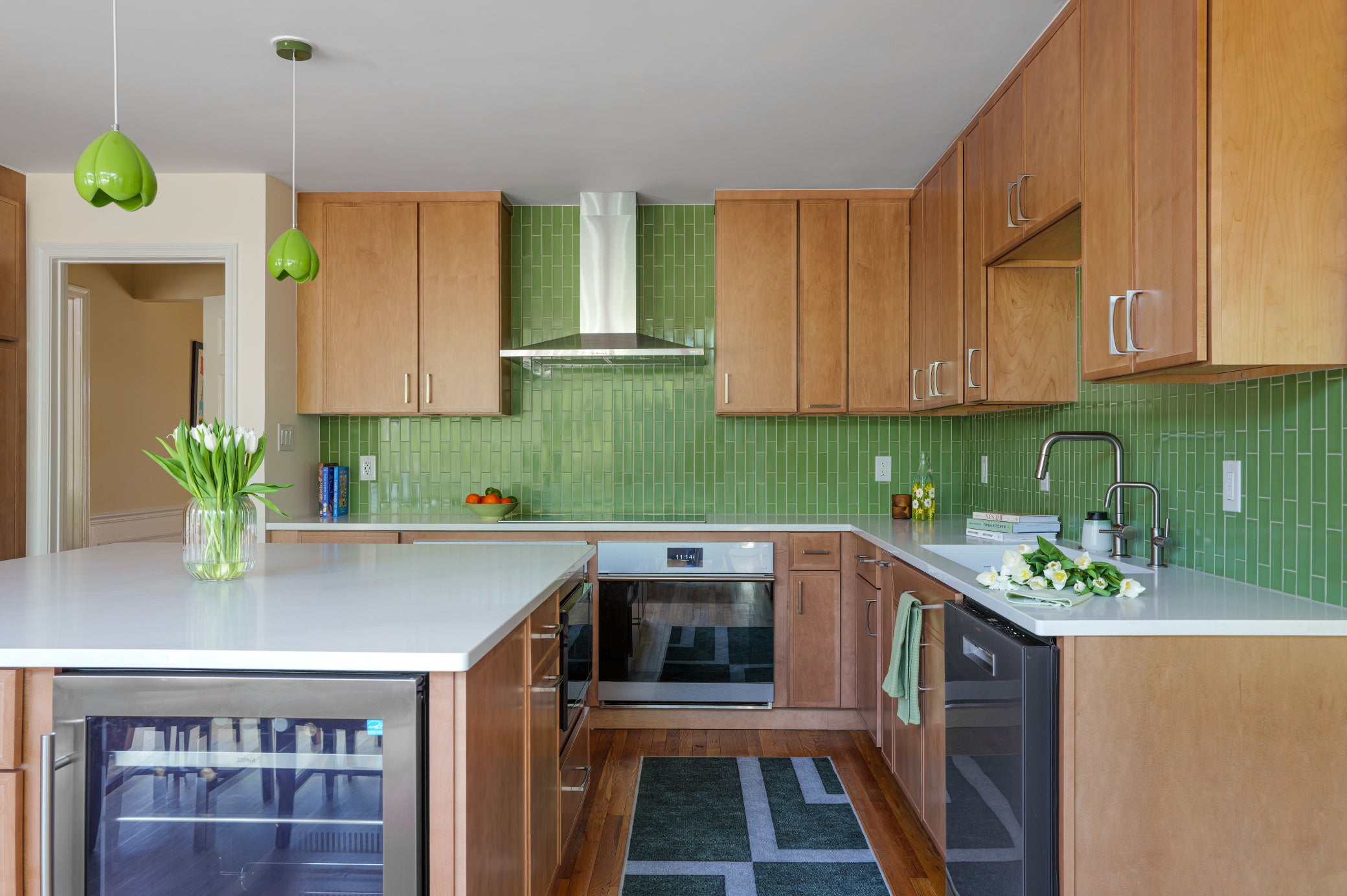Modern kitchen with wooden cabinets, green tiles, and stainless steel appliances.