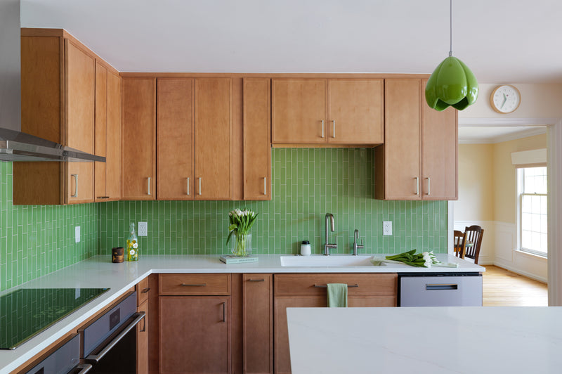 Modern kitchen with maple wooden cabinets, green backsplash, and white countertops, brushed nickel faucet.