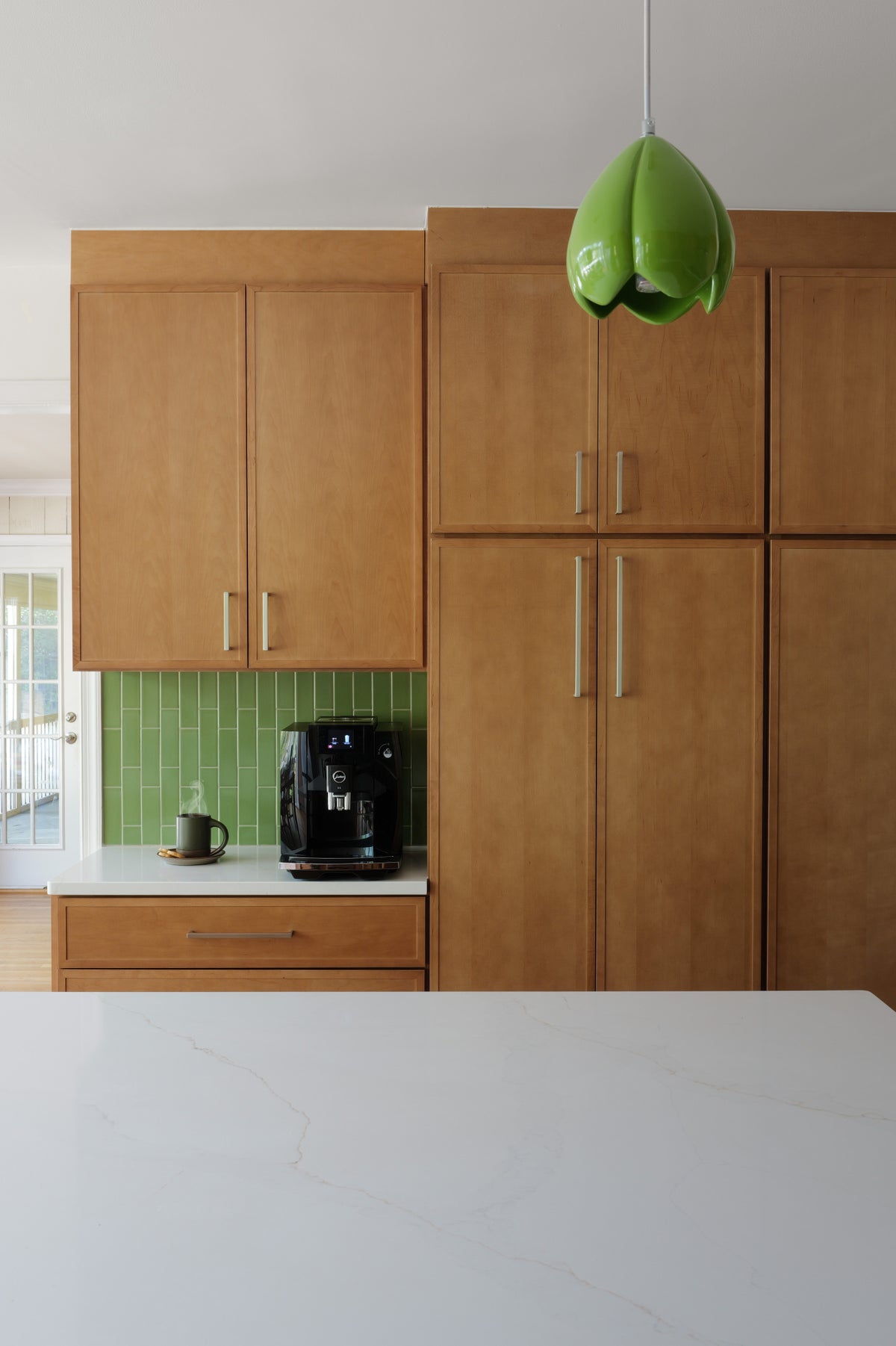 Modern kitchen with wooden cabinets, a green backsplash, green floral pendants, and a white countertop.