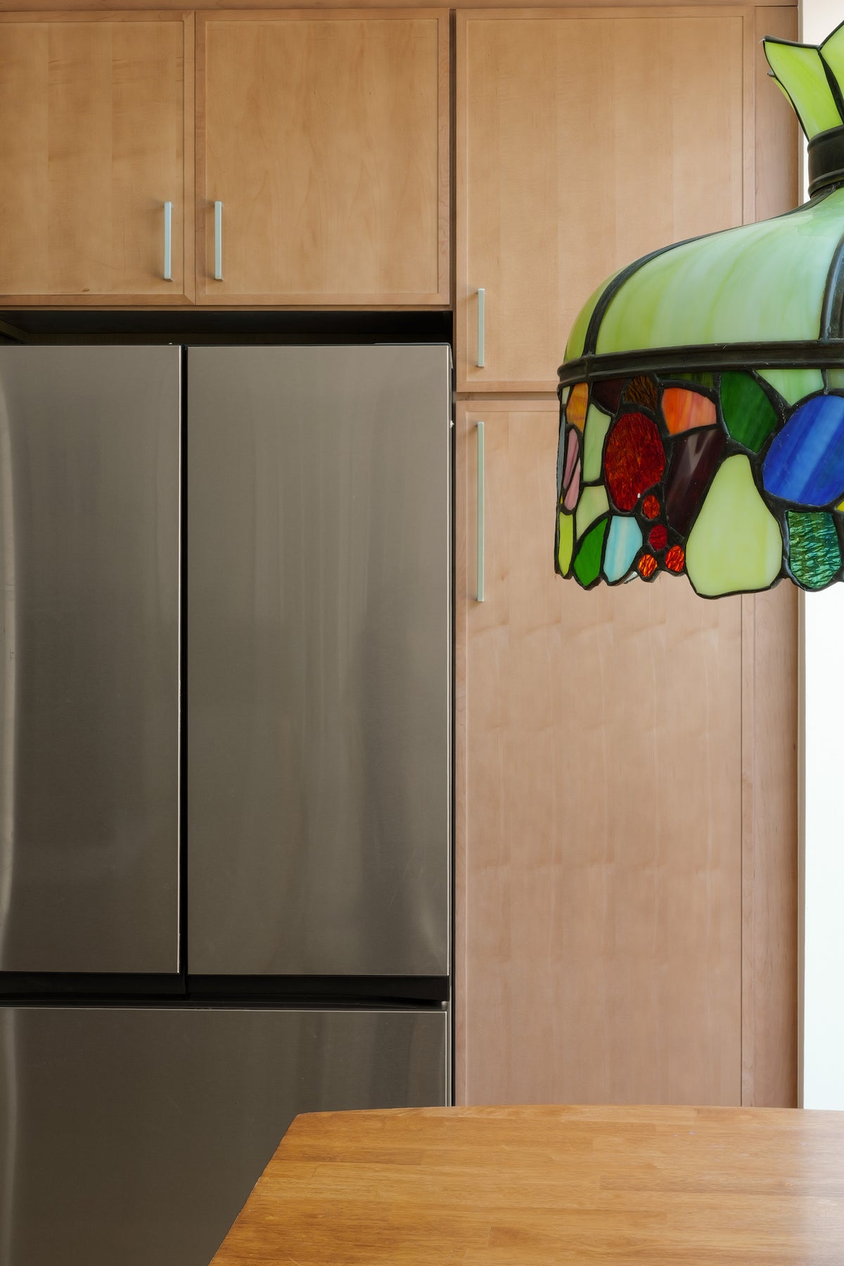 Kitchen with stainless steel refrigerator, wooden cabinets, and a colorful stained Tiffany Style glass lamp pendant.